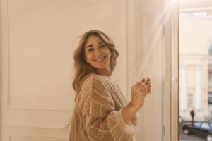 alegre mujer adulta caucasica con cabello rubio sonrie con los dientes mientras esta de pie en la habitacion