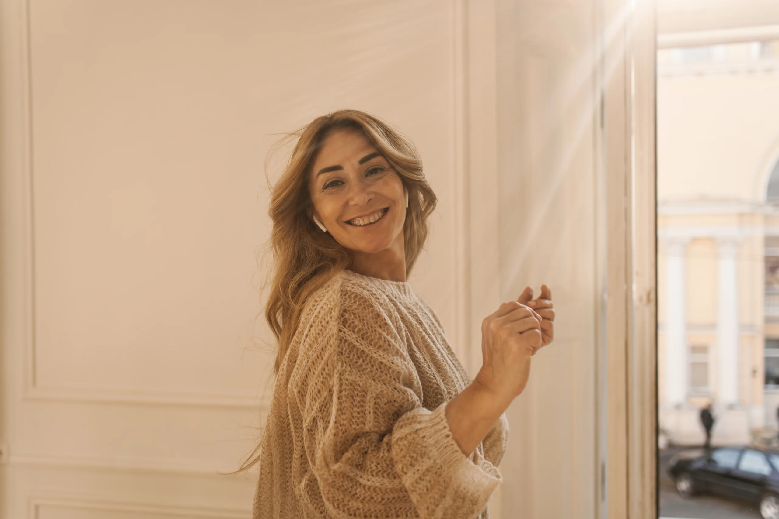 alegre mujer adulta caucasica con cabello rubio sonrie con los dientes mientras esta de pie en la habitacion